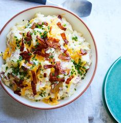 a bowl filled with mashed potatoes topped with bacon and chives next to a fork