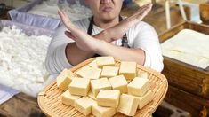 a man holding a plate full of tofu cubes in front of other food items