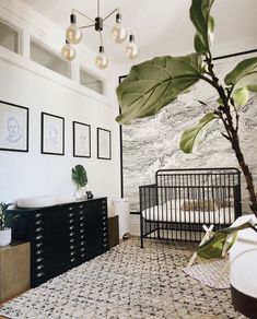 a baby crib in the corner of a room with pictures on the wall and a plant next to it