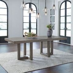 a dining room table with lights hanging from the ceiling and potted plants on top