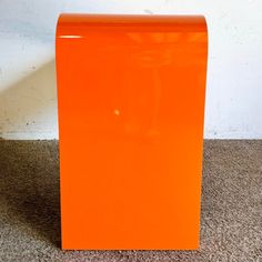 an orange box sitting on the floor in front of a white wall and brown carpet