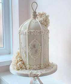 a white wedding cake with a birdcage on top and ribbon around the edges