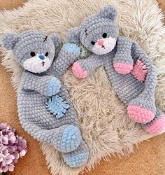 two crocheted teddy bears laying next to each other on a white rug with purple flowers