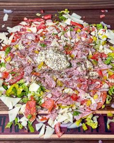 a large salad with meat, cheese and lettuce on a wooden cutting board