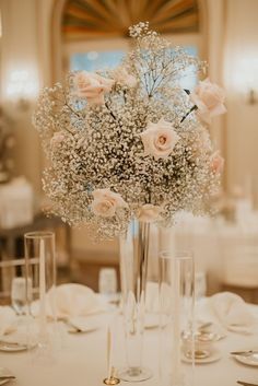 a vase filled with lots of white flowers on top of a table next to wine glasses