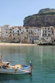 a small boat in the water next to a city on a cliff side with buildings behind it