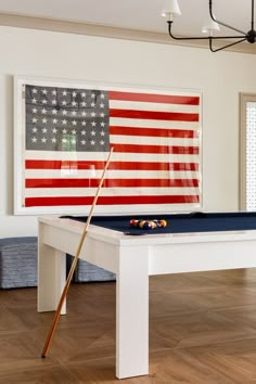 a pool table with an american flag on the wall and two cues in front of it