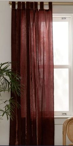 a window with a curtain hanging next to a chair and potted plant in front of it