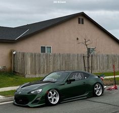 a dark green sports car parked in front of a house on the side of the road