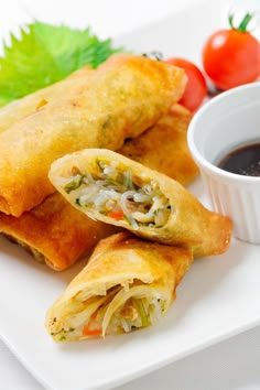 two vegetable spring rolls on a plate with dipping sauce and cherry tomatoes in the background