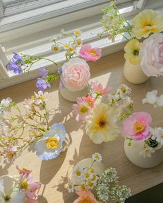 several vases filled with different types of flowers sitting on a window sill next to a window