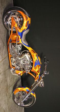 an orange and blue motorcycle with flames painted on it's side, parked next to a wall