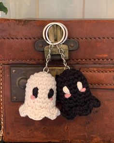 two crocheted keychains are hanging from a brown piece of luggage, one is black and the other is white