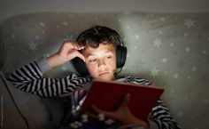 a young boy wearing headphones and listening to music while sitting on a couch with a book