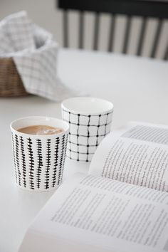 two coffee cups sitting next to an open book on top of a white countertop