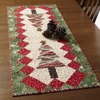 a quilted table runner with christmas trees on it and a pine cone sitting on top