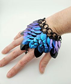 a woman's hand wearing a bracelet with blue and purple feathers on the wrist