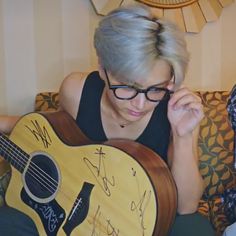 a woman sitting on top of a couch holding an acoustic guitar with autographs