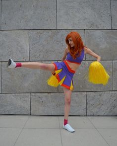 a woman with red hair is dressed up as a cheerleader in front of a stone wall