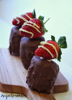 three chocolate covered strawberries sitting on top of a wooden board