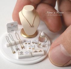 there is a display of jewelry on a white table with a hand holding it up