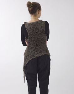 a woman standing in front of a white wall wearing black pants and a knitted vest