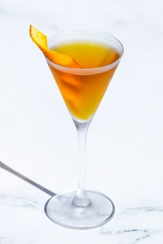 an orange slice in a martini glass on a marble counter top with a spoon nearby