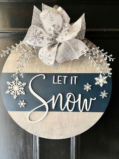 a wooden sign that says let it snow on the front door with white snowflakes