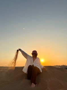 a person sitting in the sand with their arms spread out and hair blowing in the wind