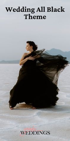 a woman in a black dress sitting on the snow with her arms around her body