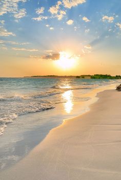 the sun is setting over the water at the beach with white sand and blue skies