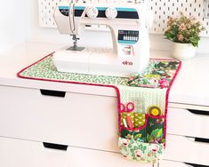 a sewing machine sitting on top of a white dresser next to flowers and potted plants