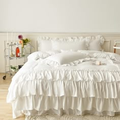 a white bed with ruffles and pillows on top of it in a room