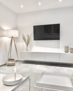 a living room with white furniture and a flat screen tv mounted on the wall above it