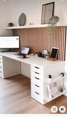 a white desk topped with a computer monitor next to a plant and a laptop on top of a wooden table