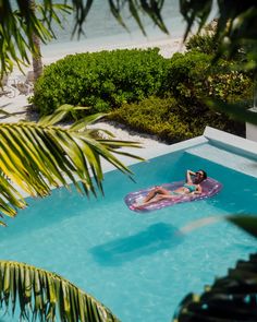 a woman laying on an inflatable raft next to a pool surrounded by greenery