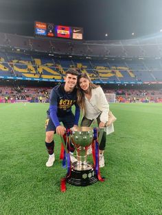 a man and woman posing for a photo with a trophy in front of an empty stadium