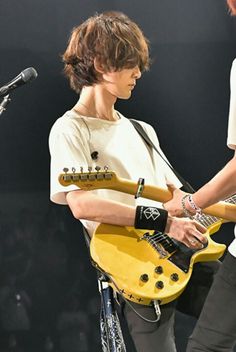 two young men are playing guitars on stage