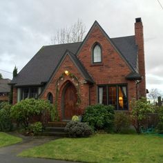 a red brick house with green bushes and shrubs around the front door on a cloudy day