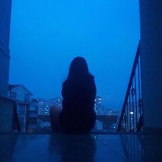 a woman sitting on the ground in front of a building with her back to the camera