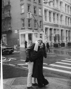 a man and woman standing on the sidewalk in front of a tall building, with their arms around each other