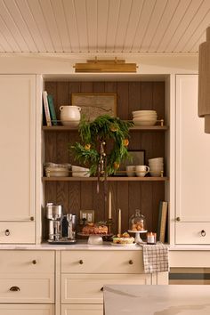 a kitchen with white cupboards and wooden shelves filled with dishes on top of them