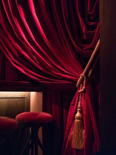 a red curtain with tassels hanging from it's side in front of two stools