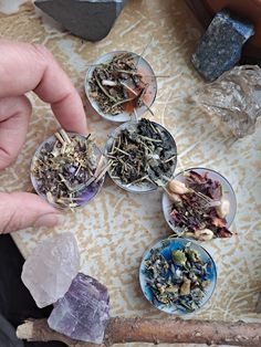 a person is picking up some tea in small bowls on a table with rocks and crystals