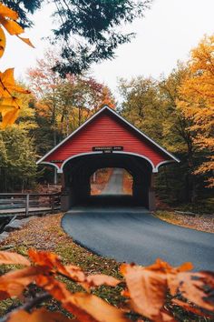 a red covered bridge surrounded by trees and leaves