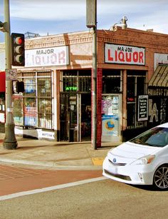 a small white car is parked in front of liquor stores on the corner of a street