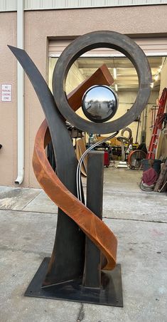 a metal sculpture sitting on top of a parking lot next to a garage door with an orange ribbon hanging from it's center