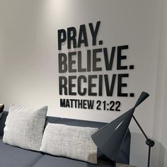 a couch with pillows and a lamp in front of a wall that says pray believe receive