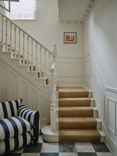 there is a blue and white striped chair next to the stairs in this house with black and white checkered flooring