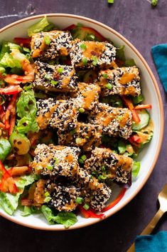 a white bowl filled with salad covered in sesame seeds and chicken meats on top of lettuce